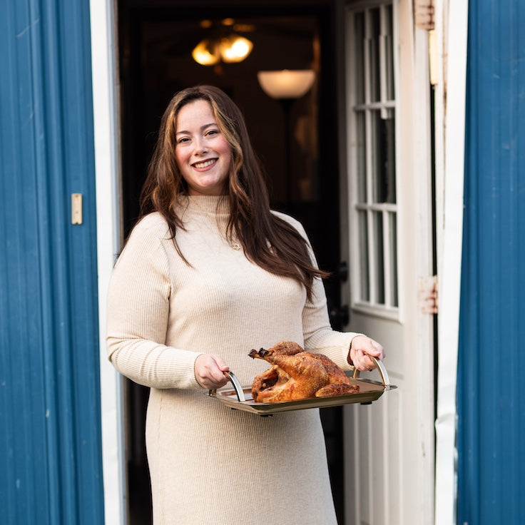 Woman holding a roasted chicken in front of a blue building